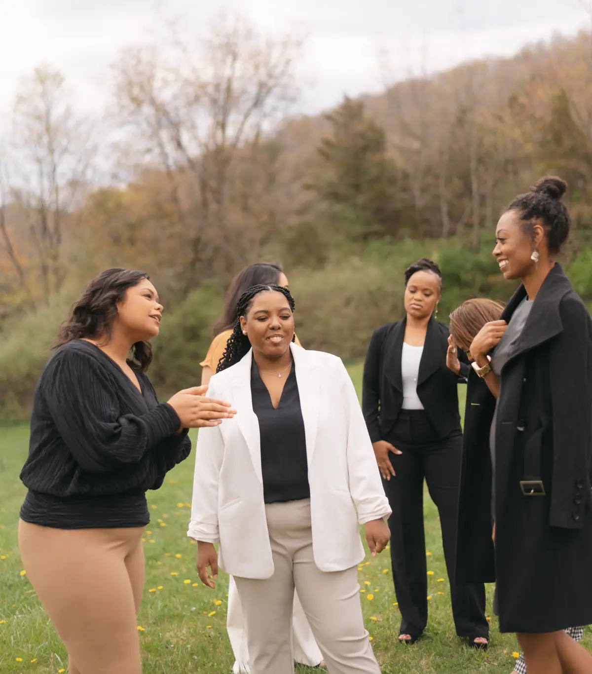 Black women in white and black blazers laugh together outdoors.